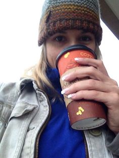 a woman drinking from a cup while wearing a beanie