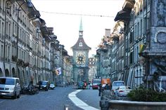 an old city street with cars parked on both sides and a clock tower in the background