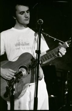 a man holding a guitar while standing in front of a microphone