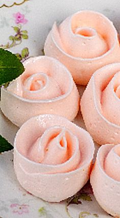 some pink frosted donuts on a white plate with green leaves and flowers in the background