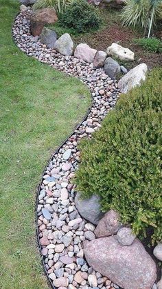 a garden with rocks and plants in the center, along side it is a gravel path