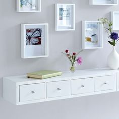 a white shelf with flowers and pictures on the wall