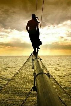 a man standing on the end of a boat in the ocean at sunset or dawn