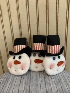 two snowmen wearing hats and boots on top of a wooden table in front of a striped wall