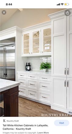 a kitchen with white cabinets and an island in front of a refrigerator freezer that is built into the wall