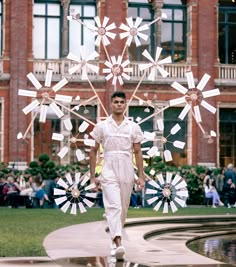 a man walking down a runway in front of a building with paper windmills on it