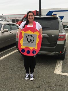 a woman standing in a parking lot holding a sign with an image of a pacman on it