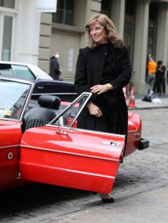 a woman standing next to an old red car