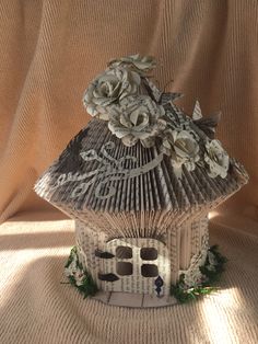 a house made out of book pages with flowers on top