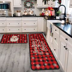 two christmas themed kitchen mats in the middle of a kitchen with white cabinets and black counter tops