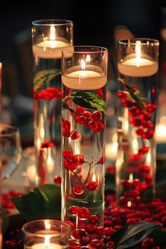 candles are lit in glass vases with red berries and greenery on the table