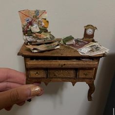 a hand holding a miniature wooden table with money on it and a clock sitting on top