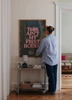 a woman standing in front of a poster on a wall next to a table with a lamp