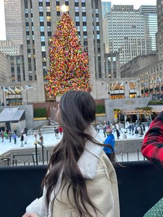 two girls are looking at a christmas tree in the middle of a city square with people walking around