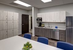 an office kitchen with stainless steel appliances and blue chairs in front of a white table