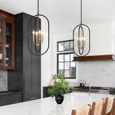 a kitchen with marble counter tops and wooden chairs in front of an island that has two hanging lights over it