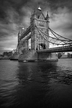 black and white photograph of the tower bridge in london, england with dark clouds overhead