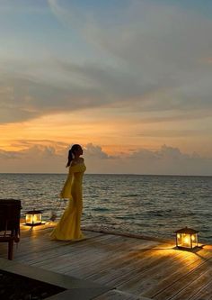 a woman in a long yellow dress standing on a dock with candles lit up next to her