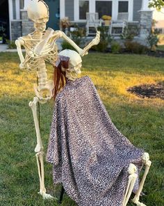 a skeleton sitting next to a woman in a dress on the grass with her head down