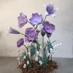 purple and white flowers in a vase on the ground next to a planter with leaves