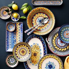 an assortment of colorful plates and bowls on a black surface with lemons in the background