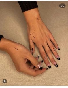 two hands with black and white nail polishes on their fingers, one holding the other's hand