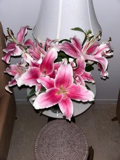 pink lilies are in a vase on a table next to a chair and lamp