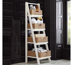 a white ladder shelf with baskets and towels on it in front of a black door