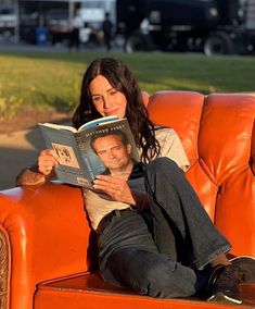 a woman sitting on top of an orange couch reading a book next to a man