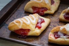 four pastries on a baking sheet with icing and strawberry jam in the middle