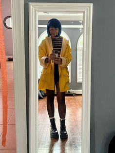 a woman standing in front of a mirror looking at her cell phone while wearing a yellow coat