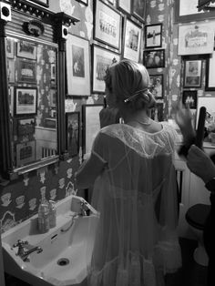 a woman is brushing her teeth in front of a mirror with pictures on the wall