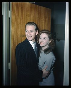 a man and woman standing next to each other in front of a wooden paneled wall