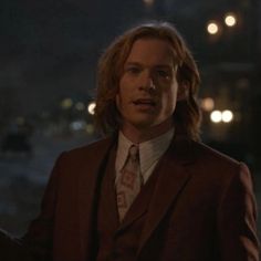 a man with long hair wearing a suit and tie standing in the street at night