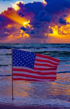 an american flag on the beach at sunset with storm clouds in the sky behind it