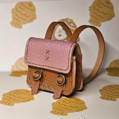 a small brown and pink purse sitting on top of a white table next to a wall