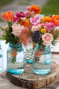 two mason jars filled with colorful flowers on top of a wooden tablecloth covered table