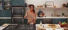 a woman standing in a kitchen preparing food on top of a stove next to an oven