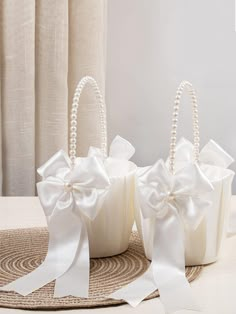 three small white baskets with bows and pearls on the handles are sitting on a table