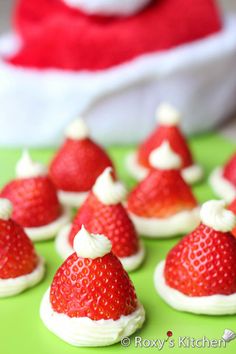 small red and white strawberries with santa hats on them are sitting on a green surface