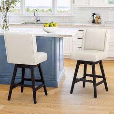 two white stools sit in front of a kitchen island with fruit on the counter