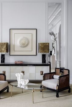 a living room with two chairs and a coffee table in front of a painting on the wall