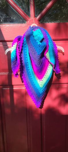 a colorful crocheted shawl hanging on a red door