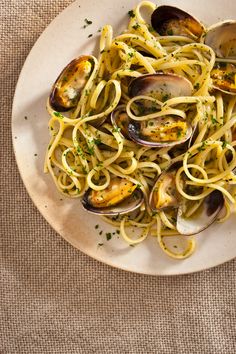 a white plate topped with pasta and clams on top of a cloth covered table