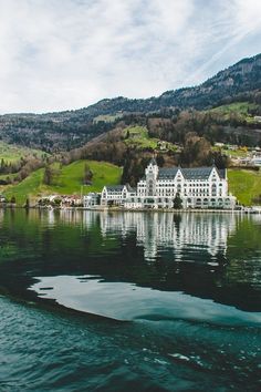 a large white house sitting on top of a lush green hillside next to a lake