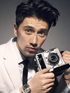 a man in a suit holding an old fashioned camera and looking at the camera lens