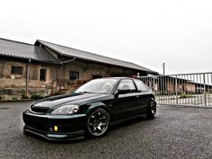 a black car parked in front of a building with a fence and gate behind it