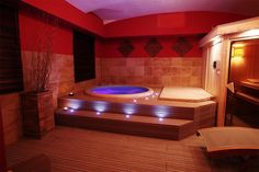 a hot tub in a room with red walls and wood flooring is lit by blue lights