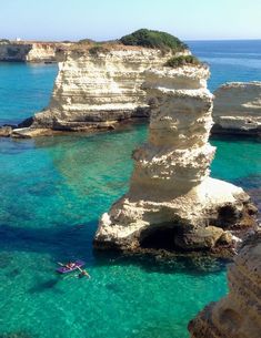 two people are swimming in the clear blue water near some white cliffs and rock formations