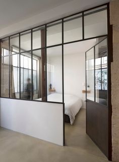 a bedroom with glass walls and a bed in the corner, as well as an open door leading to another room